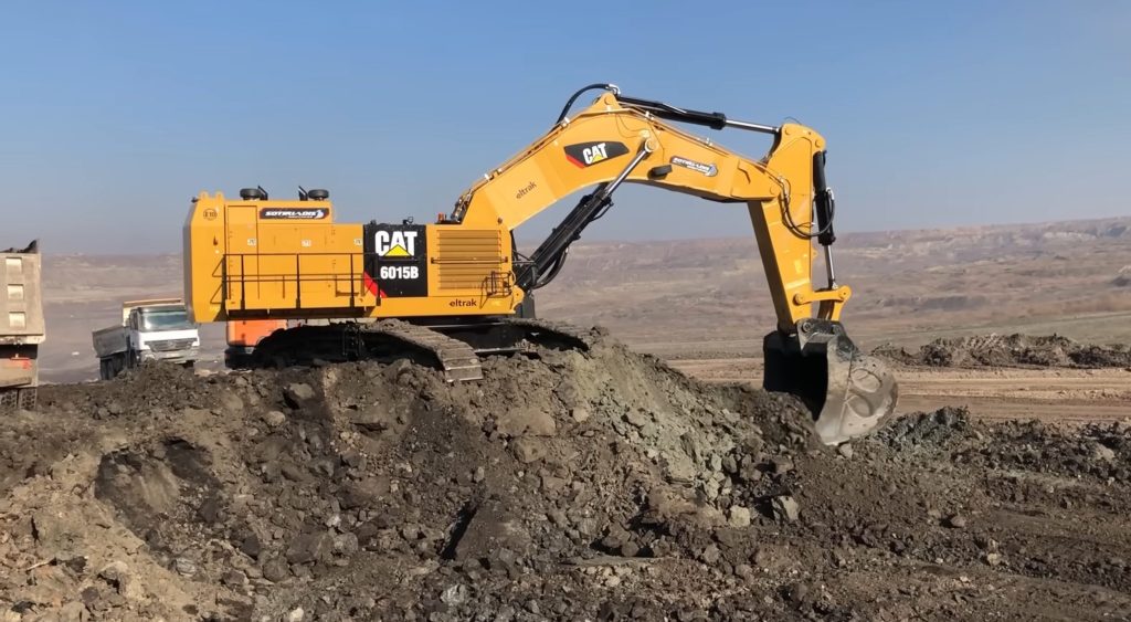 Caterpillar 6018B excavator digging soil on a ramp