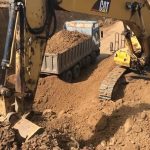 Caterpillar excavator digging earth side by trucks