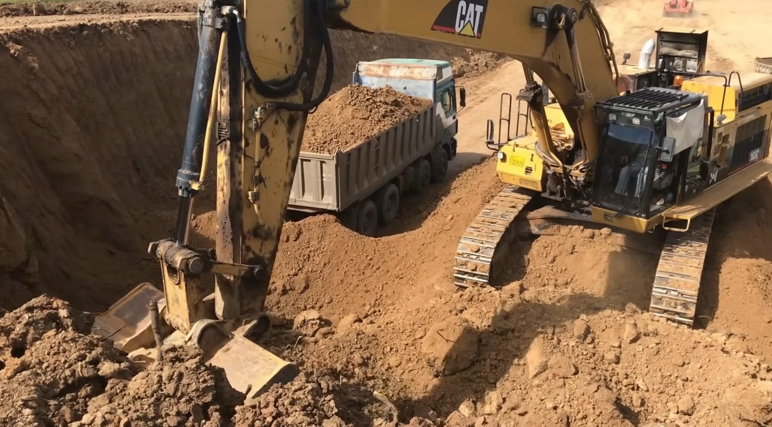 Caterpillar excavator digging earth side by trucks