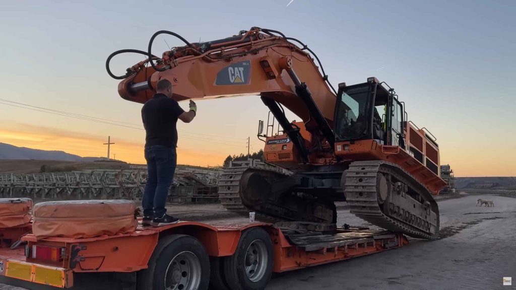 Transportation team leading excavator while loading on heavy duty trailer